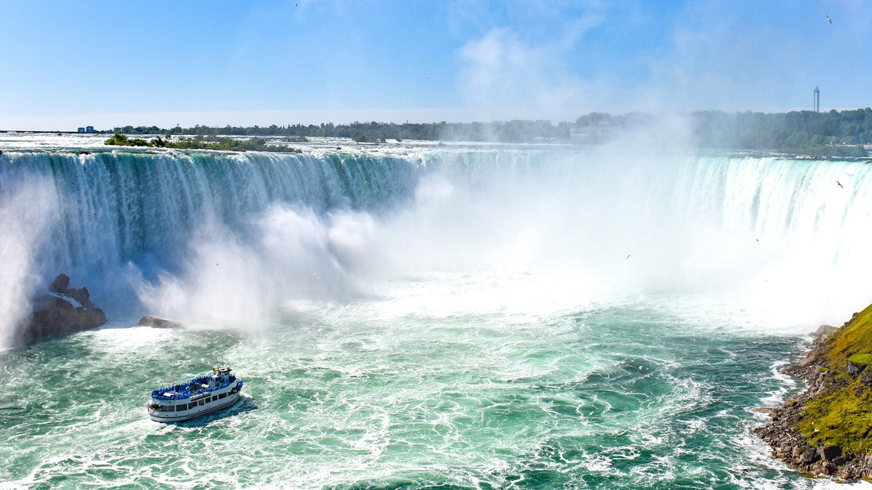 Niagara Falls view from Canada with mist rising and tourists on observation deck.