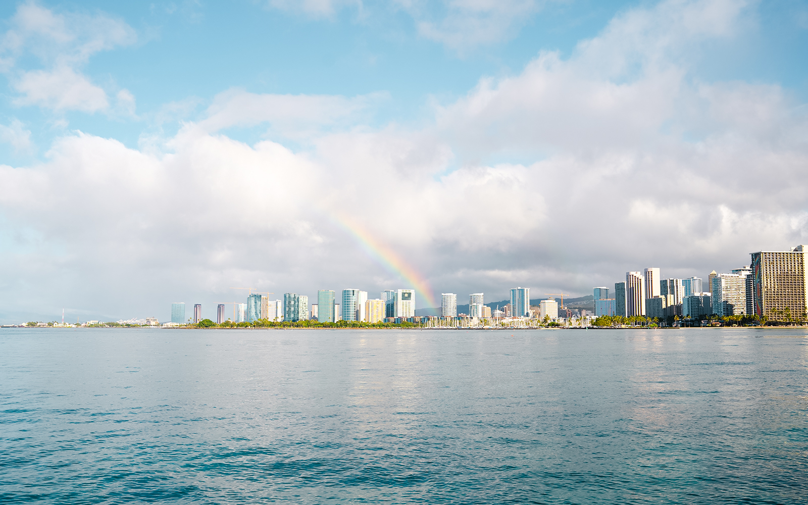 Rainbow over Honolulu skyline with ocean in foreground, Hawaii.