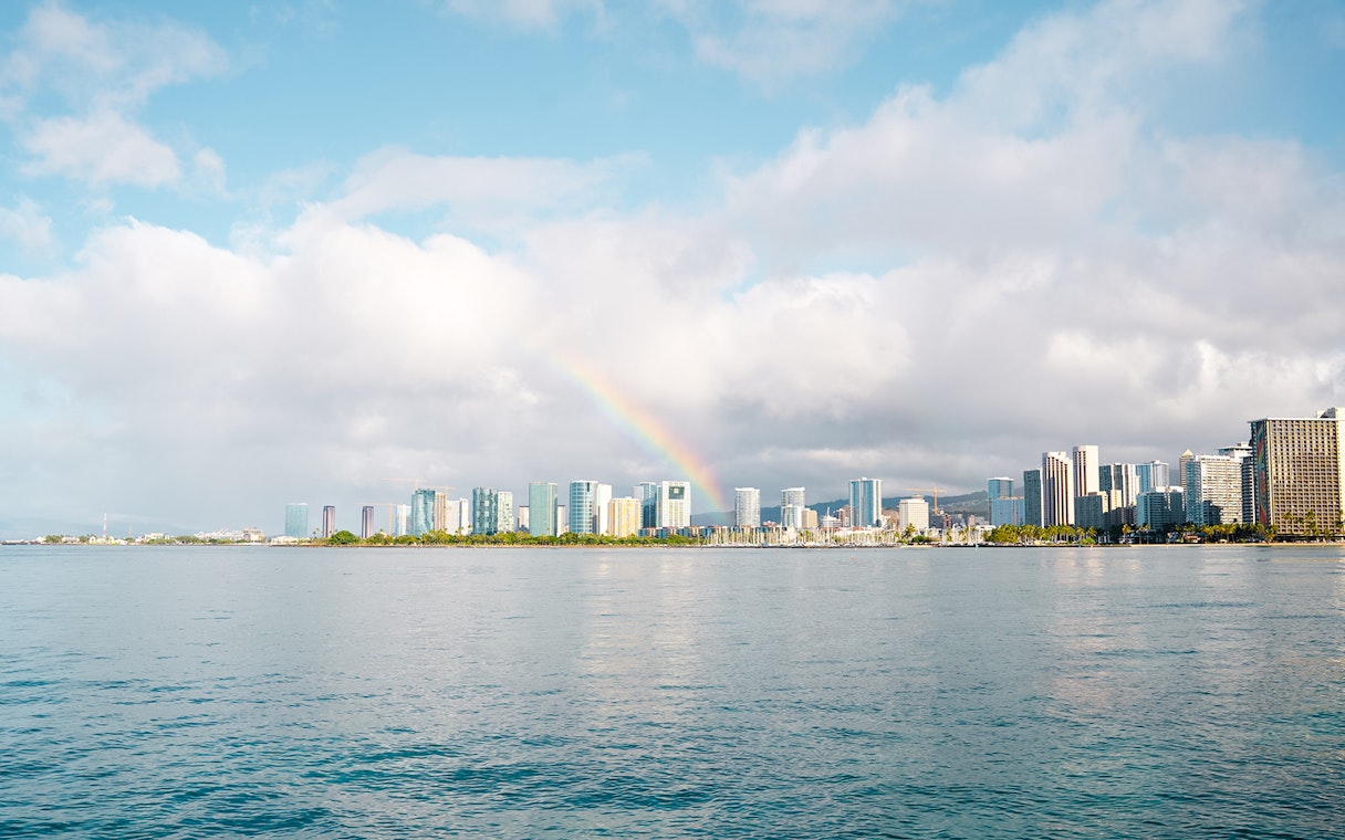 Rainbow over Honolulu skyline with ocean in foreground, Hawaii.