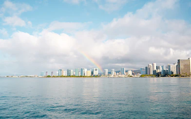 Rainbow over Honolulu skyline with ocean in foreground, Hawaii.