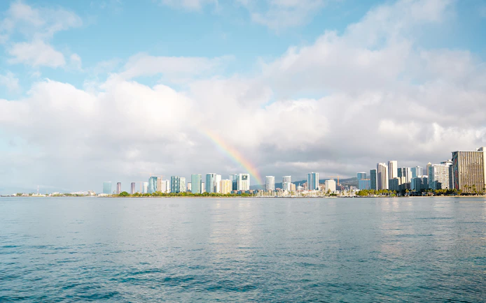 Rainbow over Honolulu skyline with ocean in foreground, Hawaii.