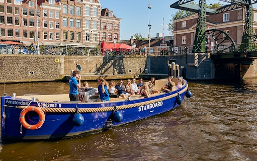 Amsterdam canal cruise boat with passengers enjoying drinks.
