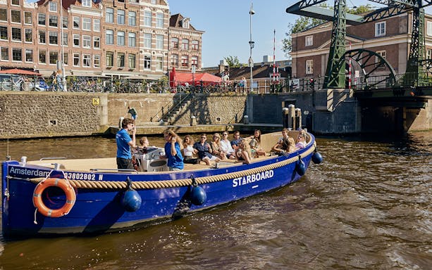 Amsterdam canal cruise boat with passengers enjoying drinks.