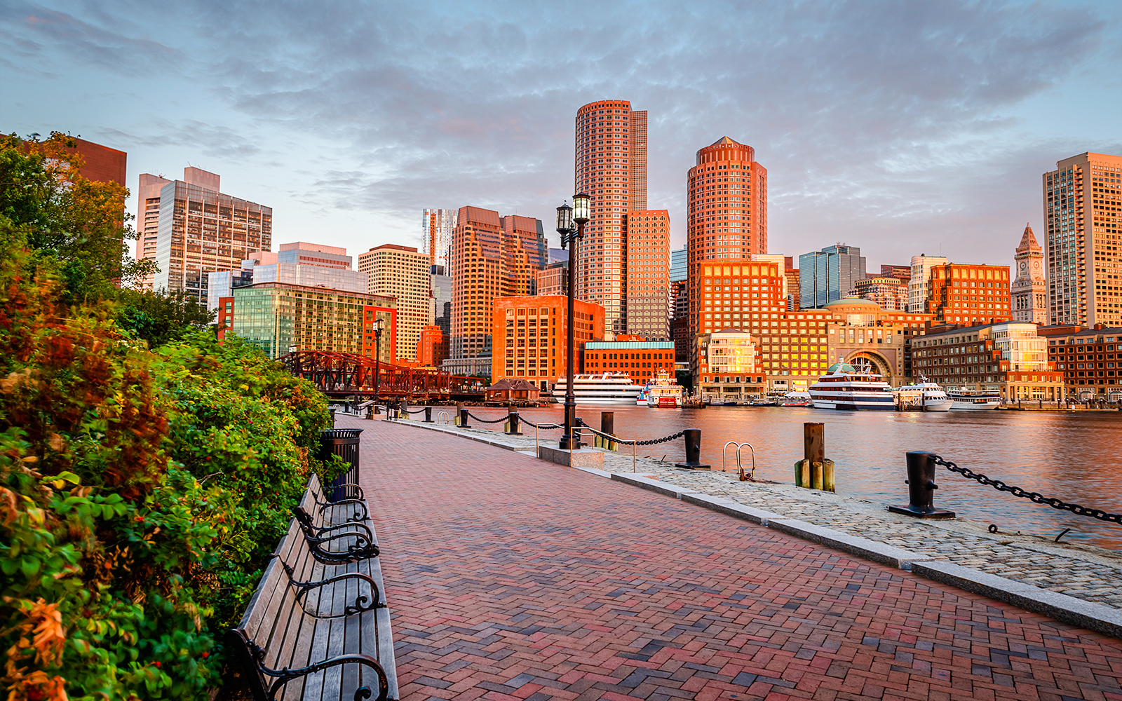 Boston Harborwalk with city skyline and waterfront at sunset.