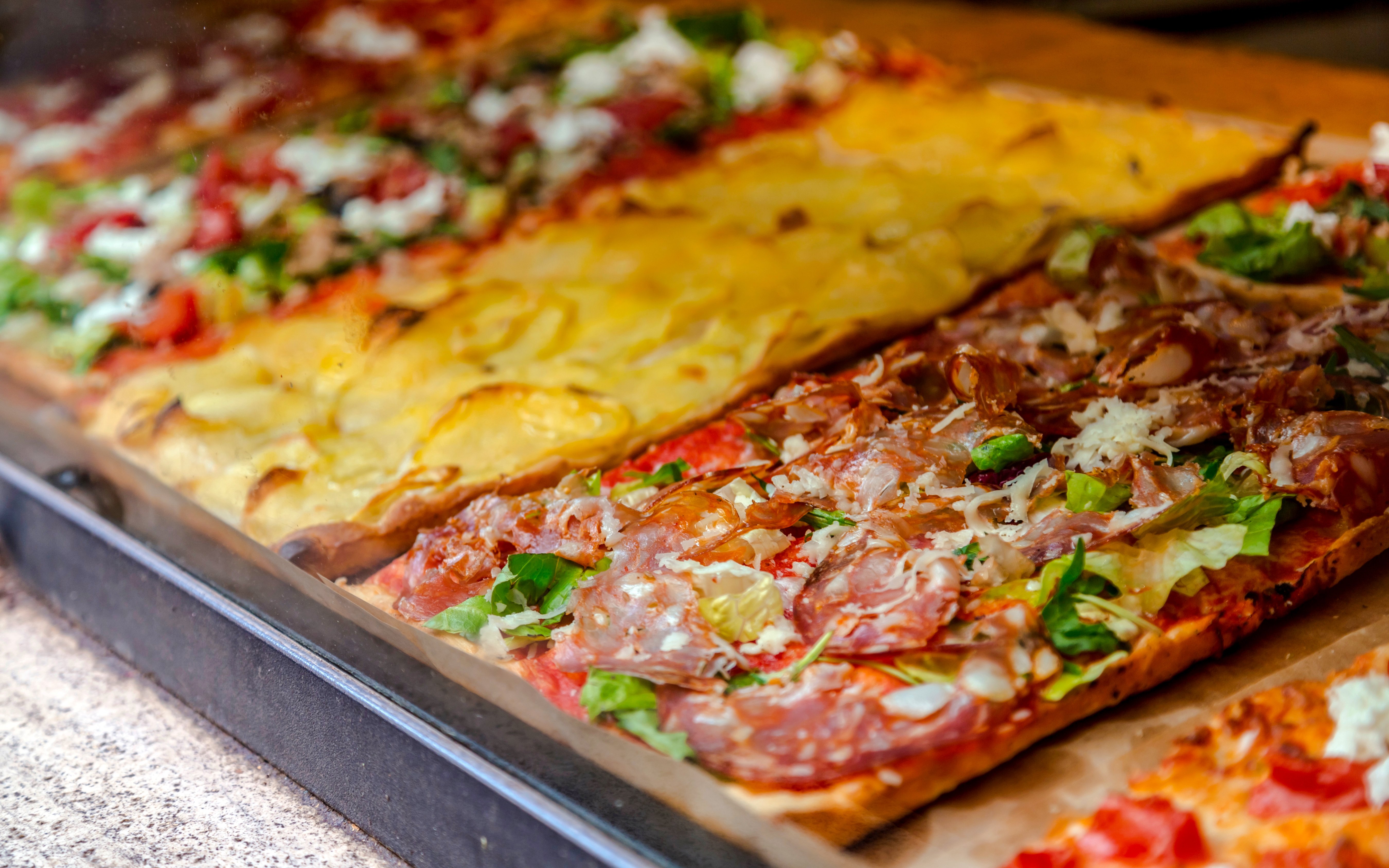 Pizza slices with various toppings on display in a Roman pizzeria.