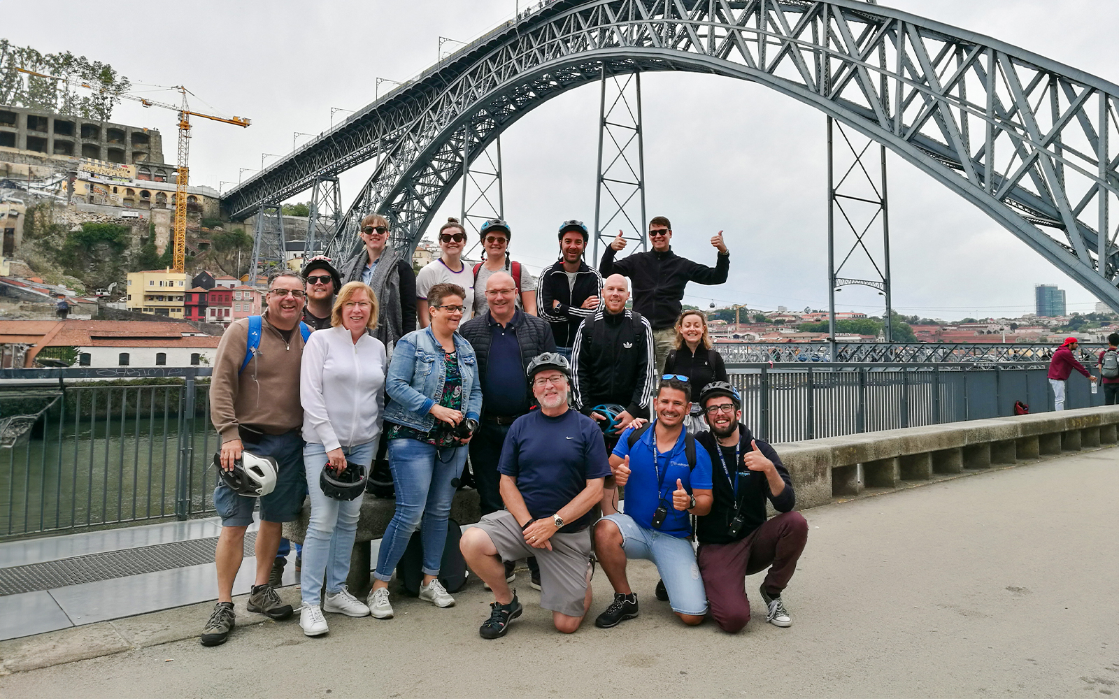 Group of cyclists posing by the Dom Luís I Bridge during a bike tour in Porto, Portugal.
