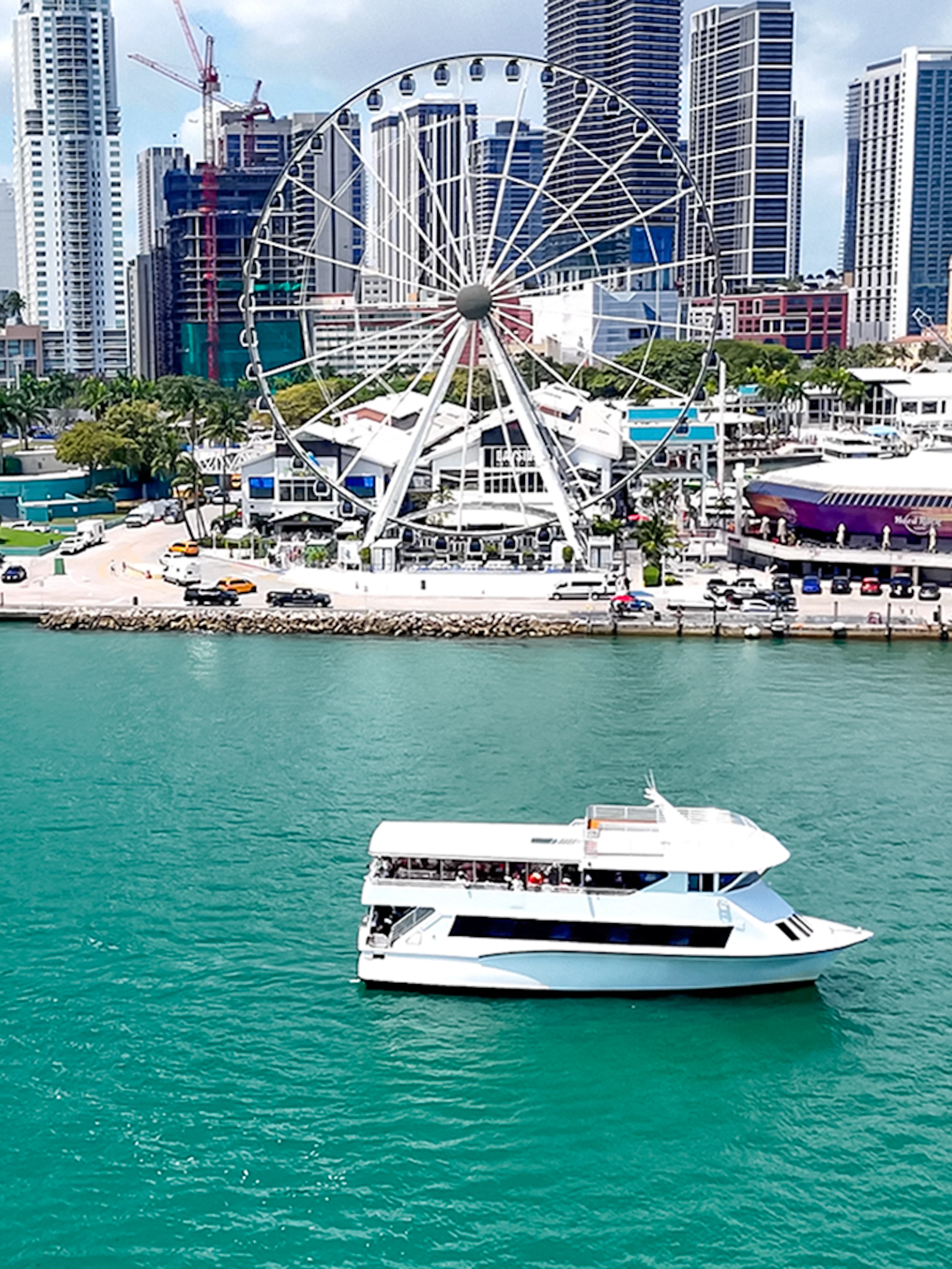 Cruise boat on Biscayne Bay with Miami skyline and Ferris wheel in the background.