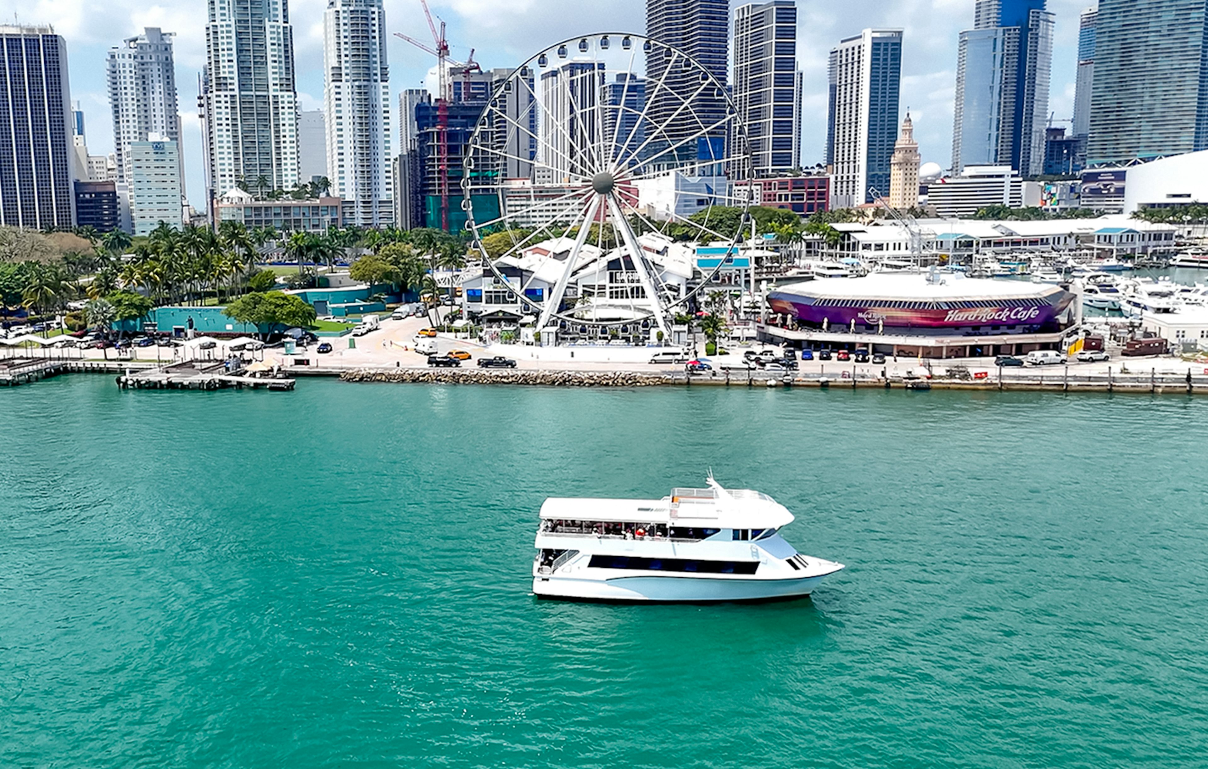 Cruise boat on Biscayne Bay with Miami skyline and Ferris wheel in the background.