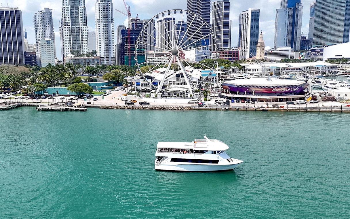 Cruise boat on Biscayne Bay with Miami skyline and Ferris wheel in the background.