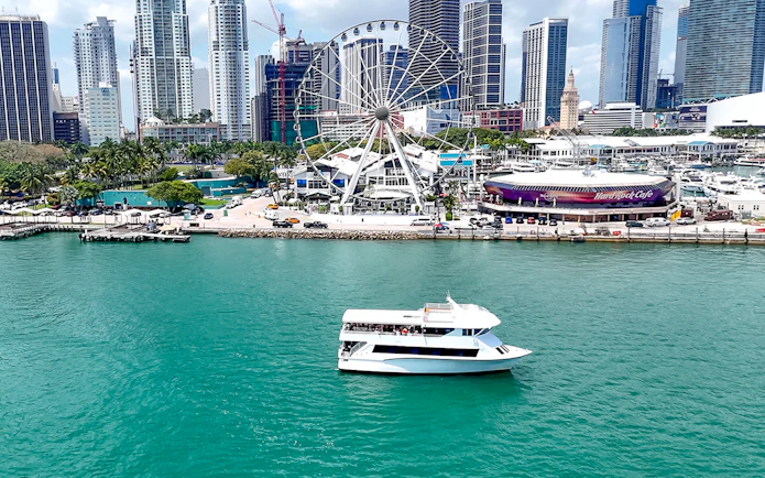 Cruise boat on Biscayne Bay with Miami skyline and Ferris wheel in the background.