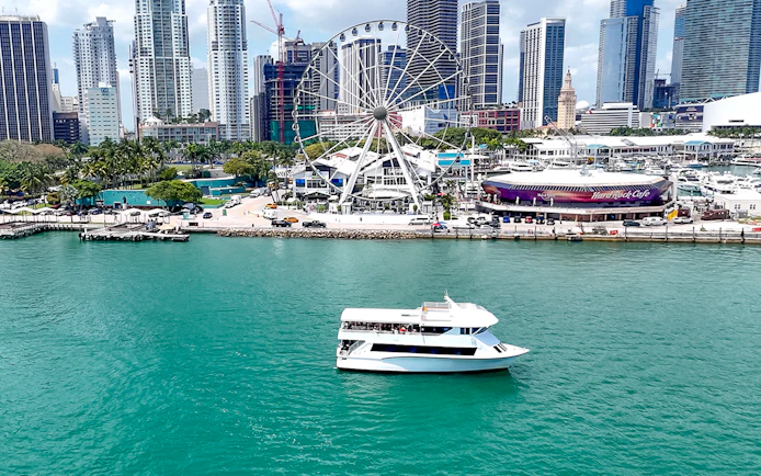 Cruise boat on Biscayne Bay with Miami skyline and Ferris wheel in the background.