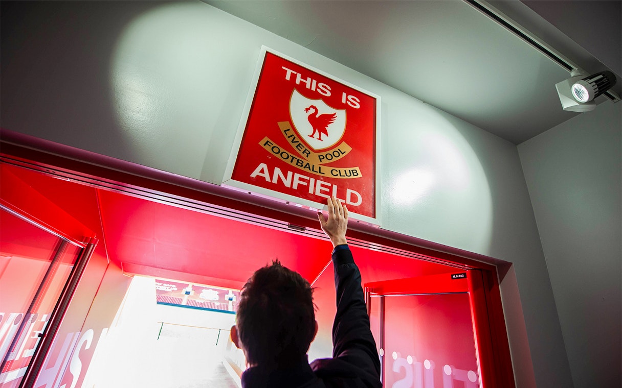 Hand reaching for "This is Anfield" sign at Liverpool FC Stadium entrance.
