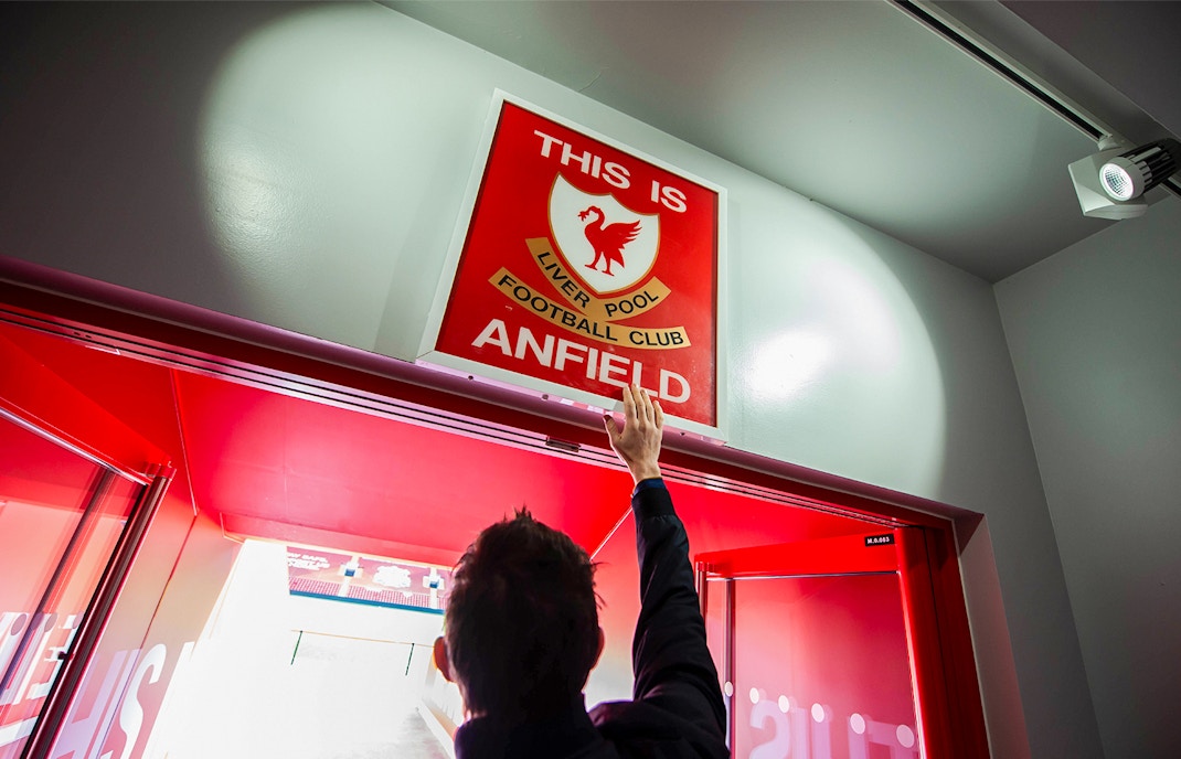 Hand reaching for "This is Anfield" sign at Liverpool FC Stadium entrance.