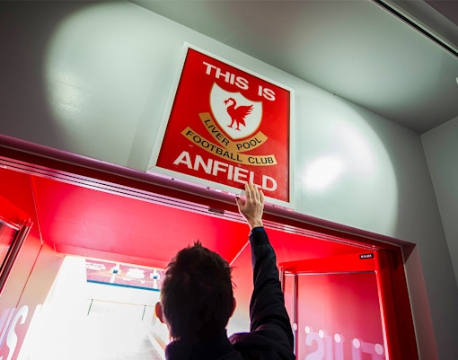 Hand reaching for "This is Anfield" sign at Liverpool FC Stadium entrance.