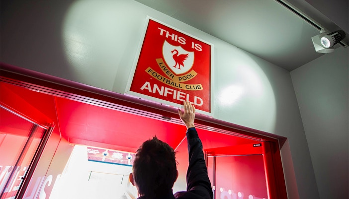 Hand reaching for "This is Anfield" sign at Liverpool FC Stadium entrance.