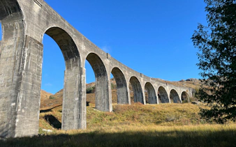 Glenfinnan Viaduct arches over scenic Scottish landscape under clear blue sky.