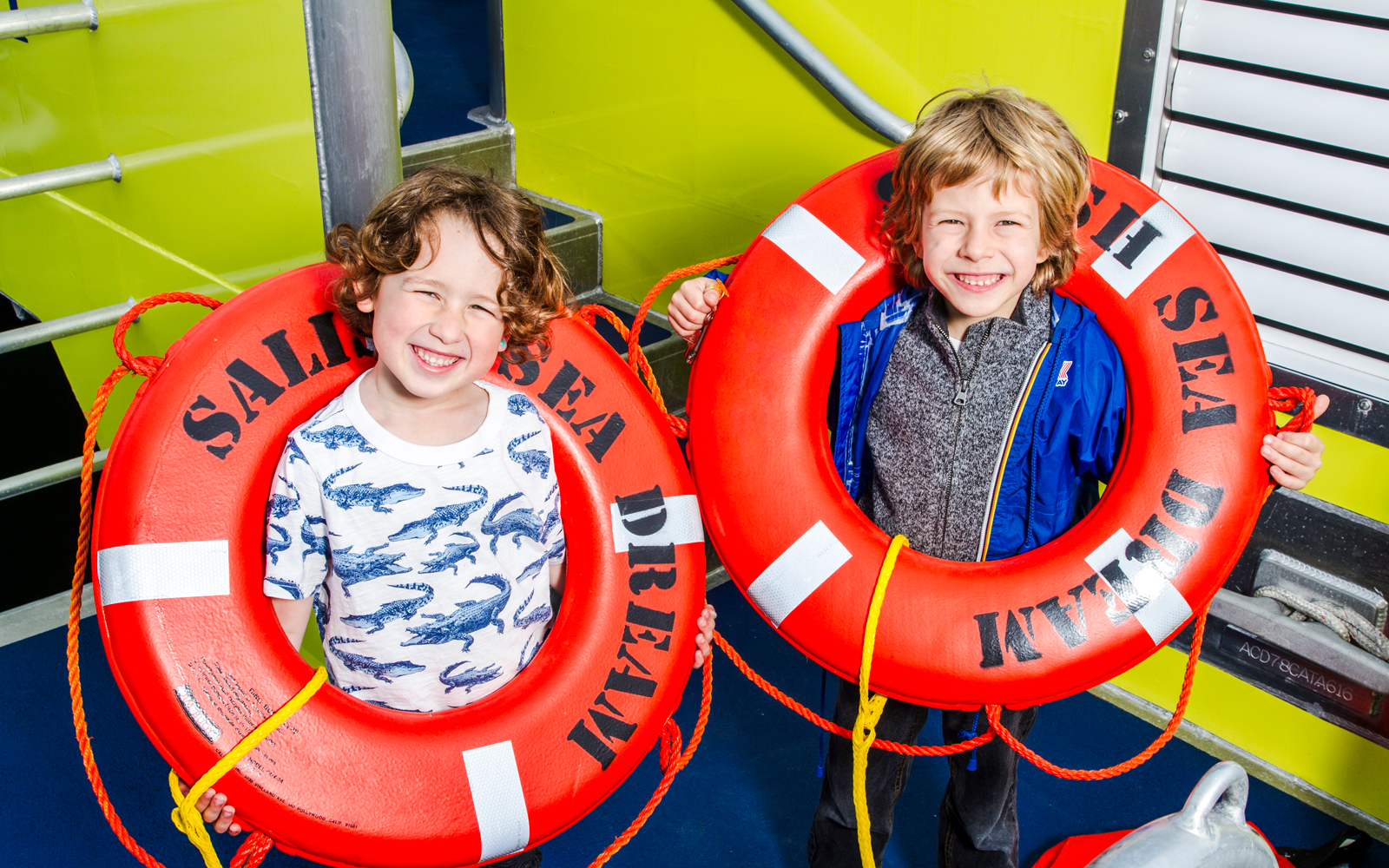 Two children holding red lifebuoys with "Sald Dream Sea" printed on them.