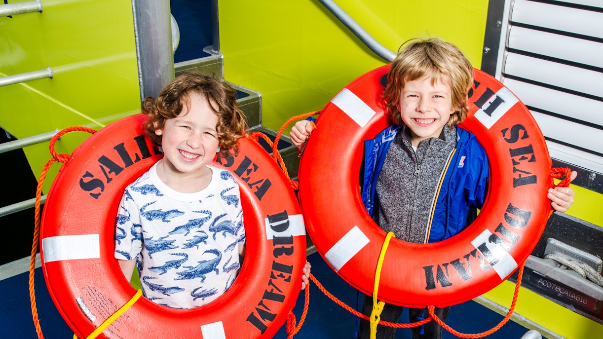 Children holding red lifebuoys with "Sald Dream Sea" during Vancouver whale watching tour.