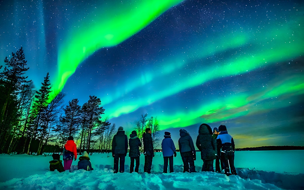 Northern lights over snowy Rovaniemi landscape with group on guided tour.