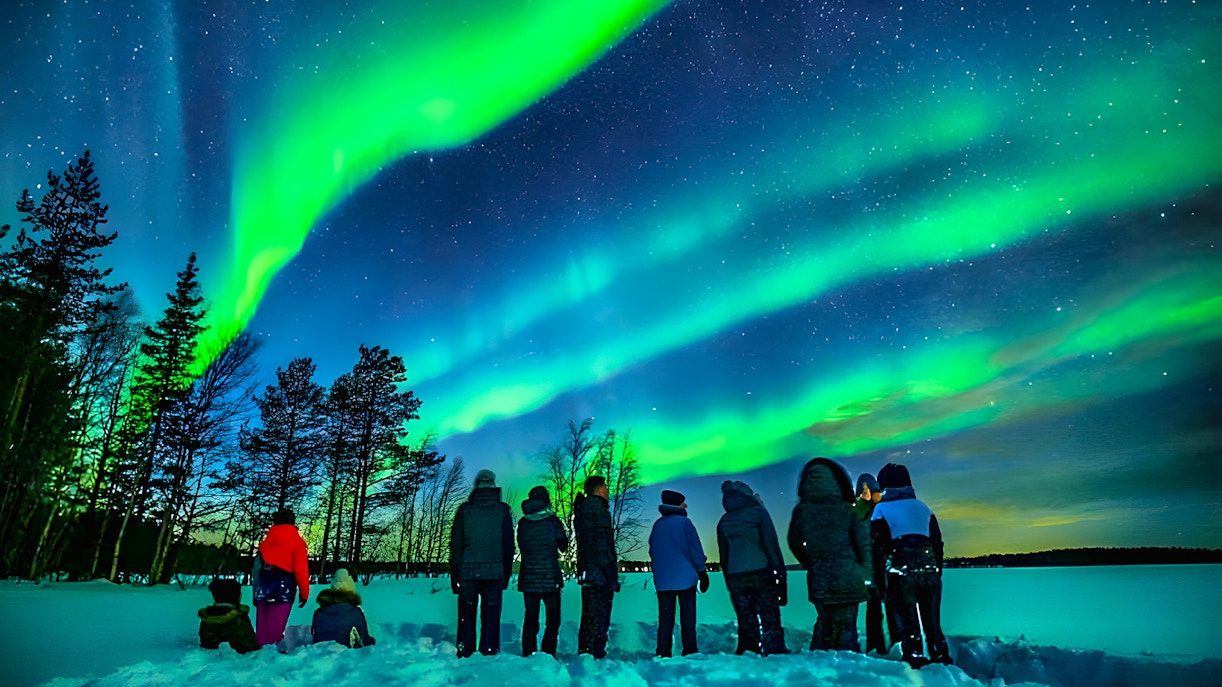 Northern lights over snowy Rovaniemi landscape with group on guided tour.