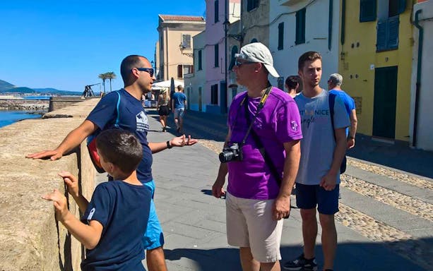 Tour group exploring Alghero Historic Center with guide by the waterfront.