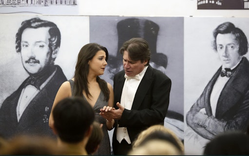 Opera singers performing with historical composer portraits in the background.