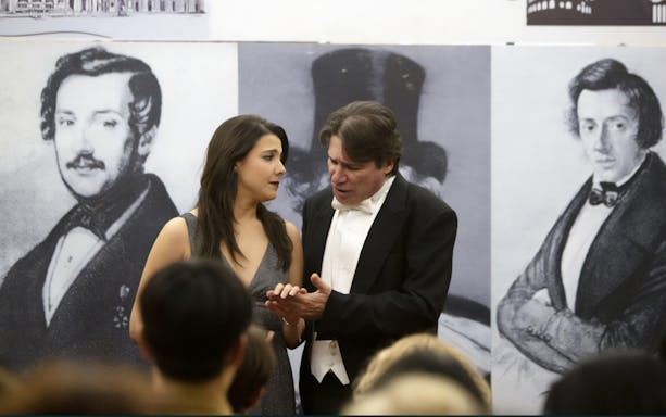 Opera singers performing with historical composer portraits in the background.