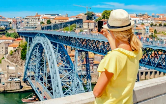Person taking photo of Dom Luís I Bridge in Porto, with cityscape in the background.