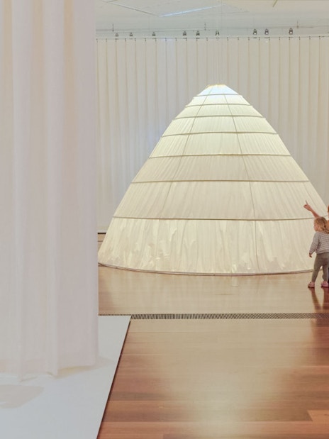 Exhibit of a silver coat and large cone structure at Martin Grant Exhibition.