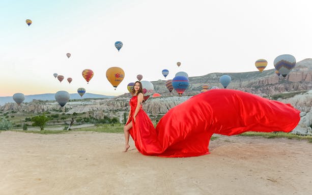 Woman in red dress with hot air balloons in Cappadocia landscape.