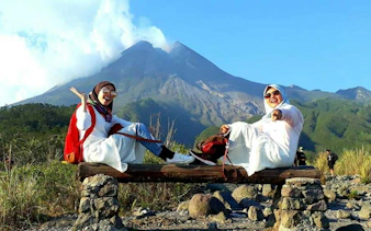 Two people sitting on a bench with Mount Merapi in the background during a Jeep Merapi Lava Tour.