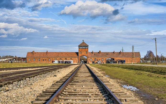 Railway tracks leading to Auschwitz-Birkenau Museum entrance under a blue sky.