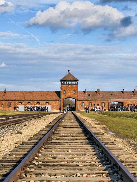 Railway tracks leading to Auschwitz-Birkenau Museum entrance under a blue sky.