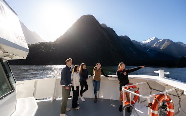 Tour group on Milford Sound cruise with guide pointing at scenic mountains, Te Anau.