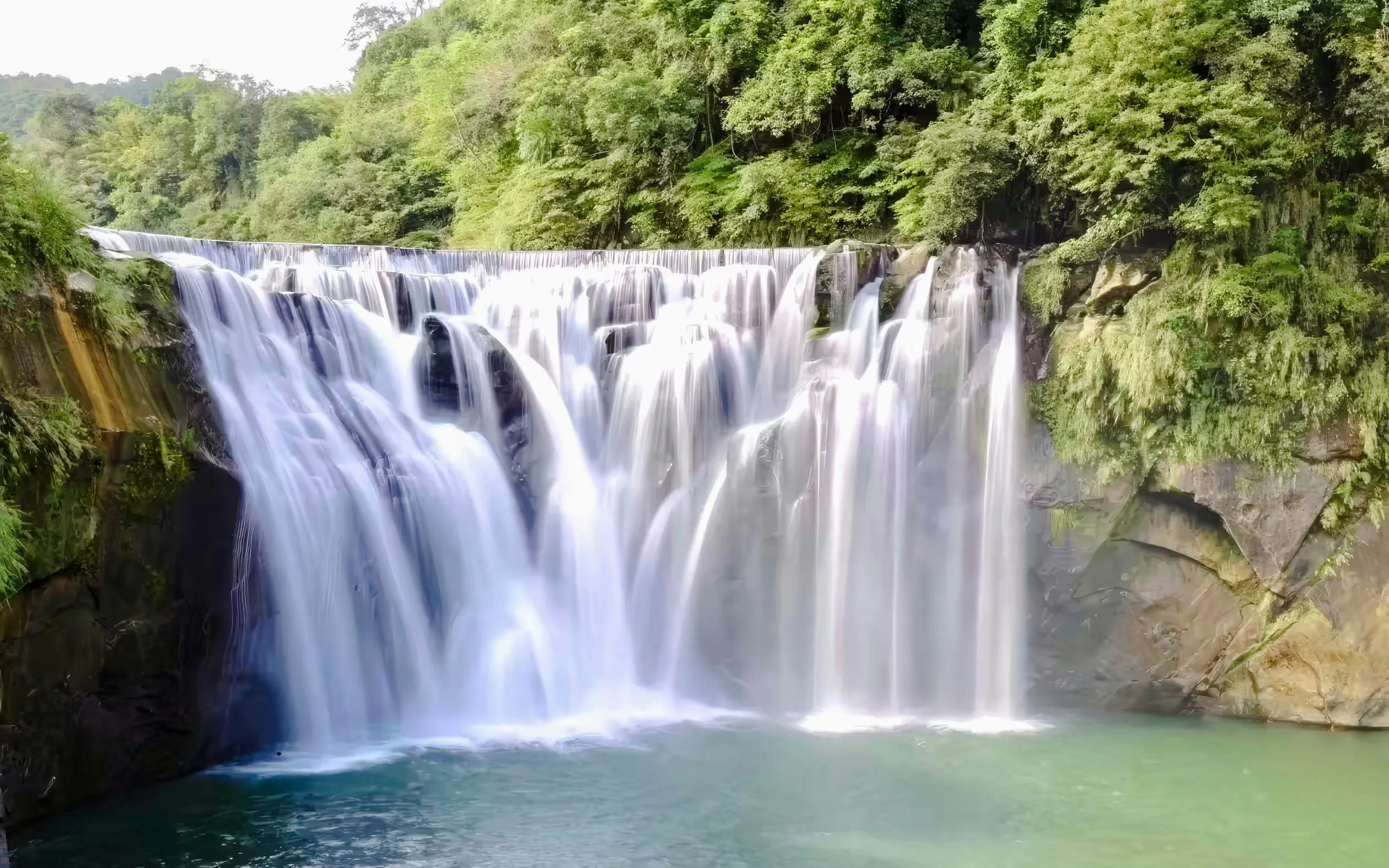 Shifen Waterfall cascading over rocks into a pool, surrounded by lush greenery in Pingxi District, Taiwan.