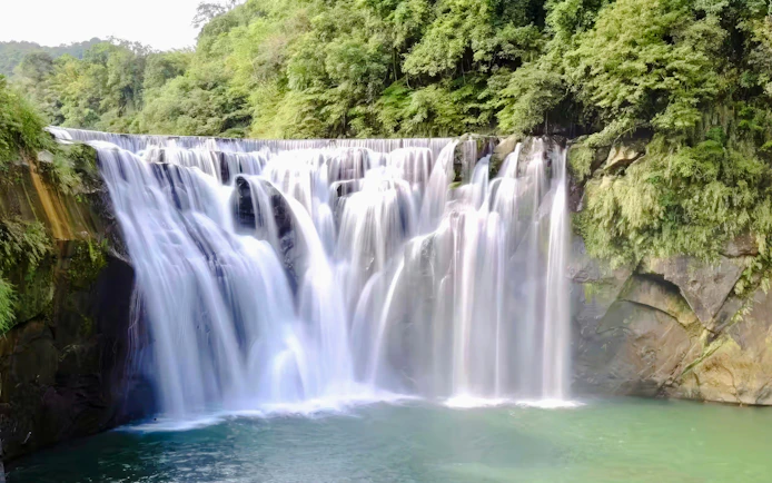 Shifen Waterfall cascading over rocks into a pool, surrounded by lush greenery in Pingxi District, Taiwan.