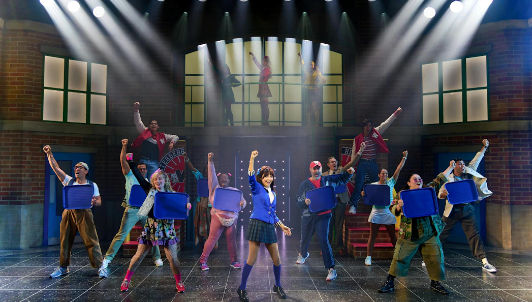 Cast performing a scene from Heathers The Musical on stage with raised fists.