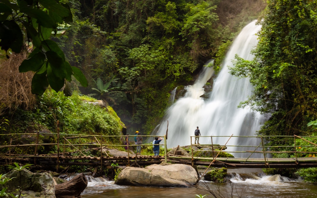 Visitors on a bamboo bridge near Pha Dok Siew waterfall in lush forest.