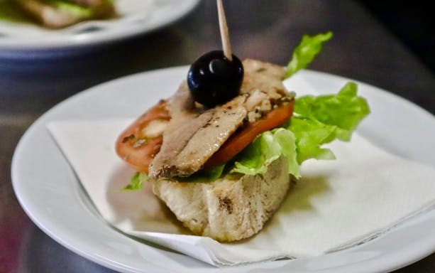 Open-faced sandwich with lettuce, tomato, fish, and olive on a Lisbon food tour.