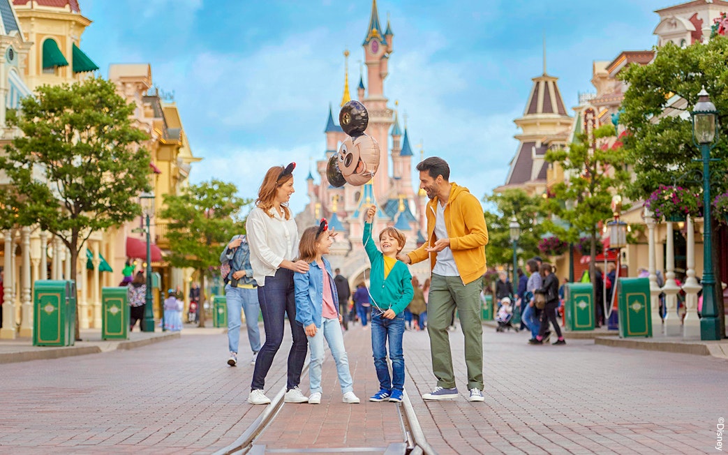 Family enjoying Disneyland Paris with balloons in front of Sleeping Beauty Castle.