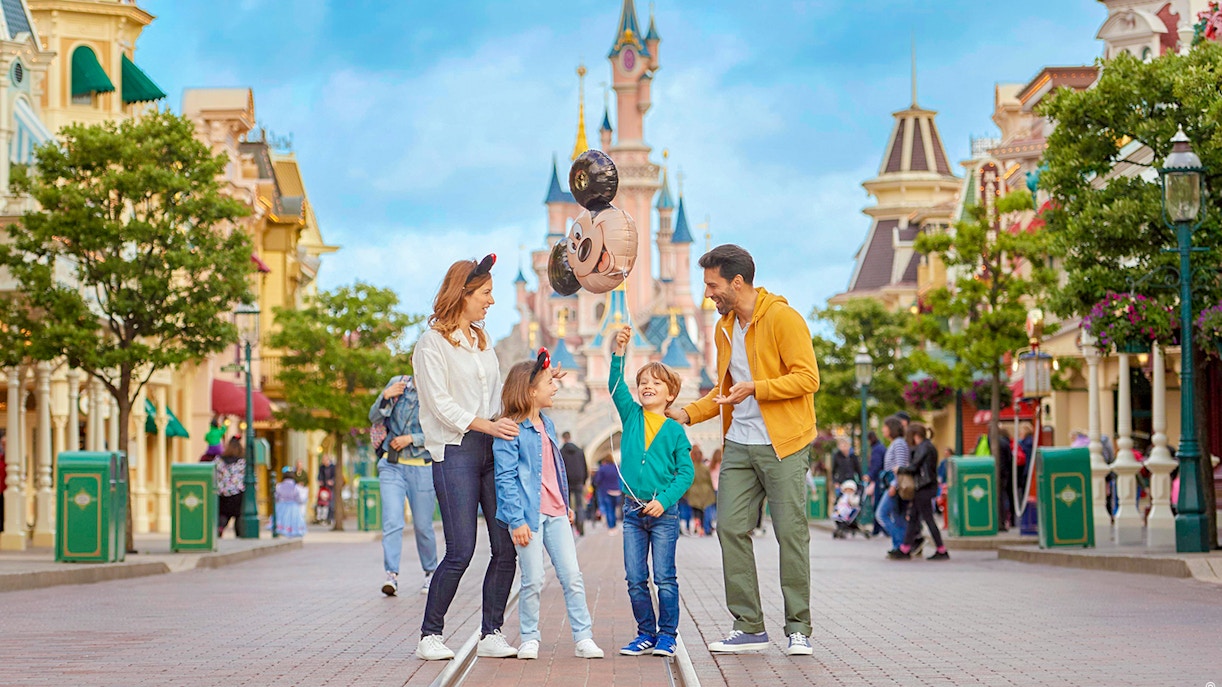 Family enjoying Disneyland Paris with balloons in front of Sleeping Beauty Castle.
