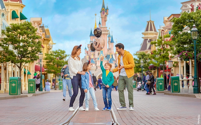 Family enjoying Disneyland Paris with balloons in front of Sleeping Beauty Castle.