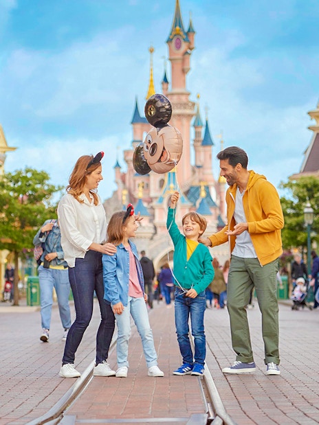 Family enjoying Disneyland Paris with balloons in front of Sleeping Beauty Castle.
