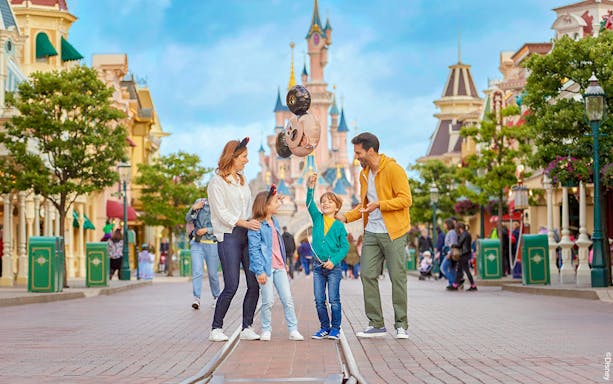Family enjoying Disneyland Paris with balloons in front of Sleeping Beauty Castle.