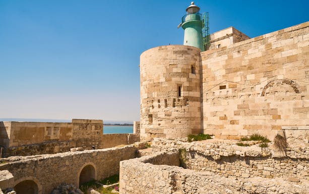 Maniace Castle stone walls and lighthouse overlooking the sea in Syracuse, Italy.