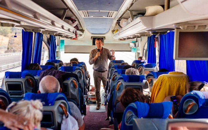 Tour guide speaking to passengers on a bus heading to Mycenae archaeological site, Peloponnese, Greece.