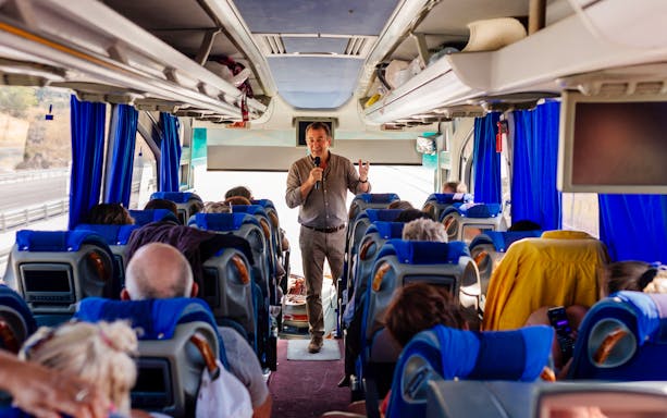 Tour guide speaking to passengers on a bus heading to Mycenae archaeological site, Peloponnese, Greece.