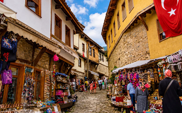 Street market in Cumalıkızık village, Turkey, with traditional stone houses and Turkish flag.