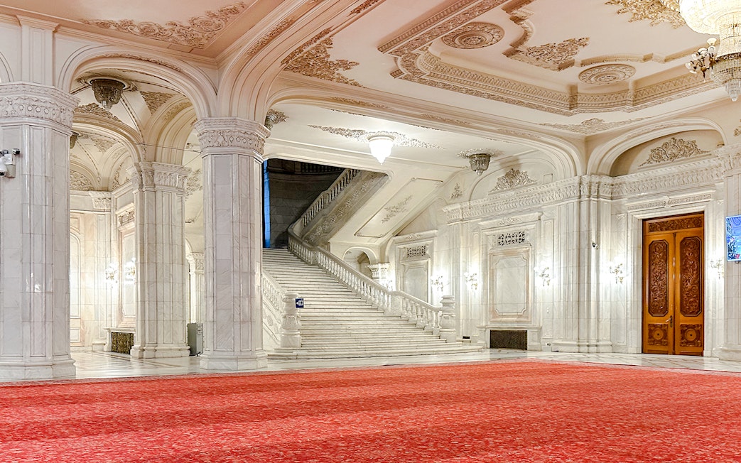 Grand staircase in the Palace of Parliament, Bucharest, with ornate ceilings and red carpet.