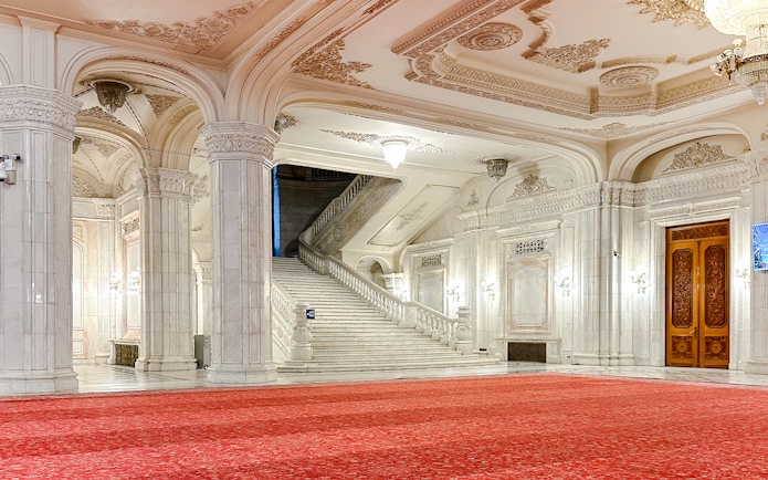Grand staircase in the Palace of Parliament, Bucharest, with ornate ceilings and red carpet.